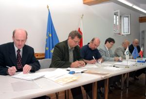 Mężczyźni siedzący przy stole podpisują dokumenty